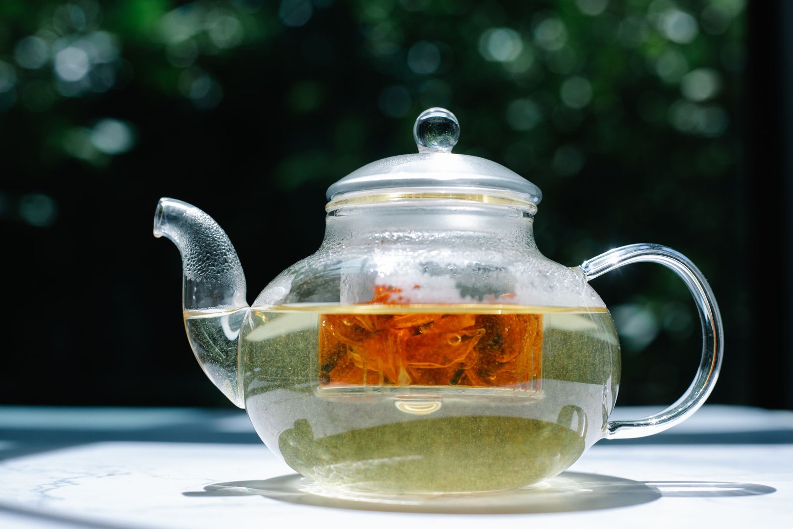 Tasse de tisane fumante à côté d'une carafe d'eau et de plantes séchées sur une table en bois